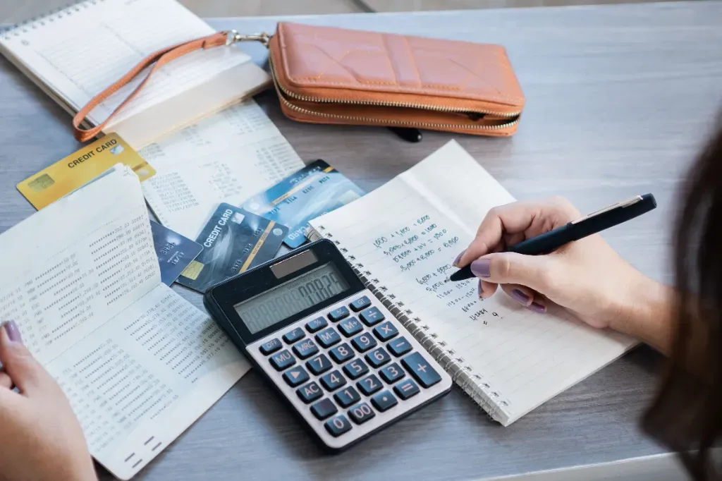 Księgowa rozlicza koszty uzyskania przychodu, zapisuje w notatniku wartości faktur, a następnie sumuje je na kalkulatorze.