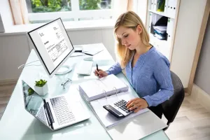 Młoda przedsiębiorczyni siedzi przy biurku i samodzielnie rozlicza wyświetlaną na monitorze fakturę VAT z zakupu na firmę.